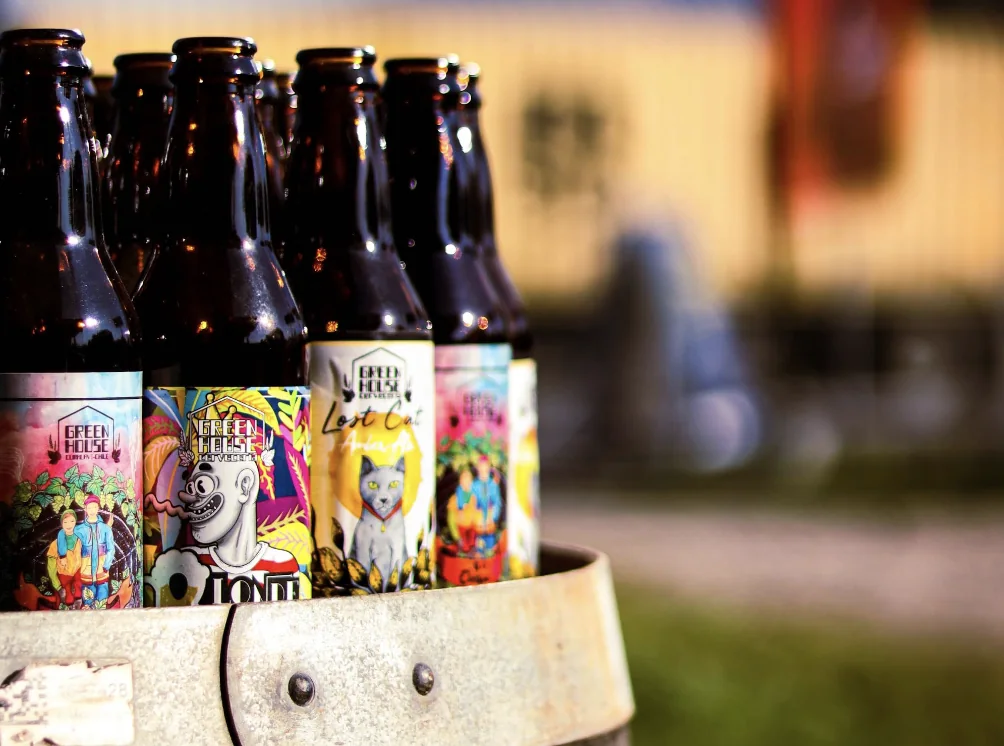 Botellas de cerveza artesanal con etiquetas ilustradas sobre un barril de madera
